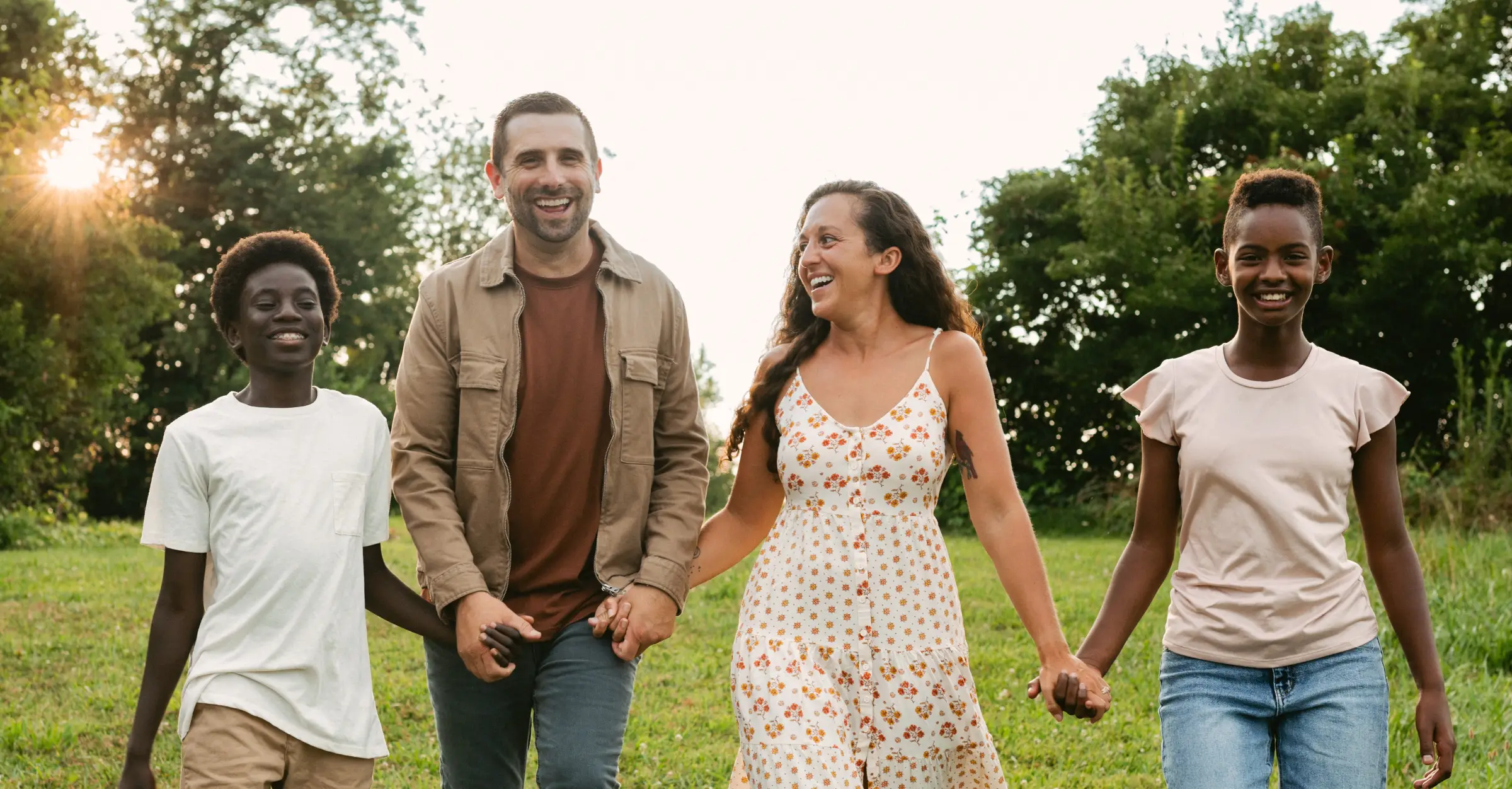 The Willet family walk hand-in-hand down a hill outside at sunset.