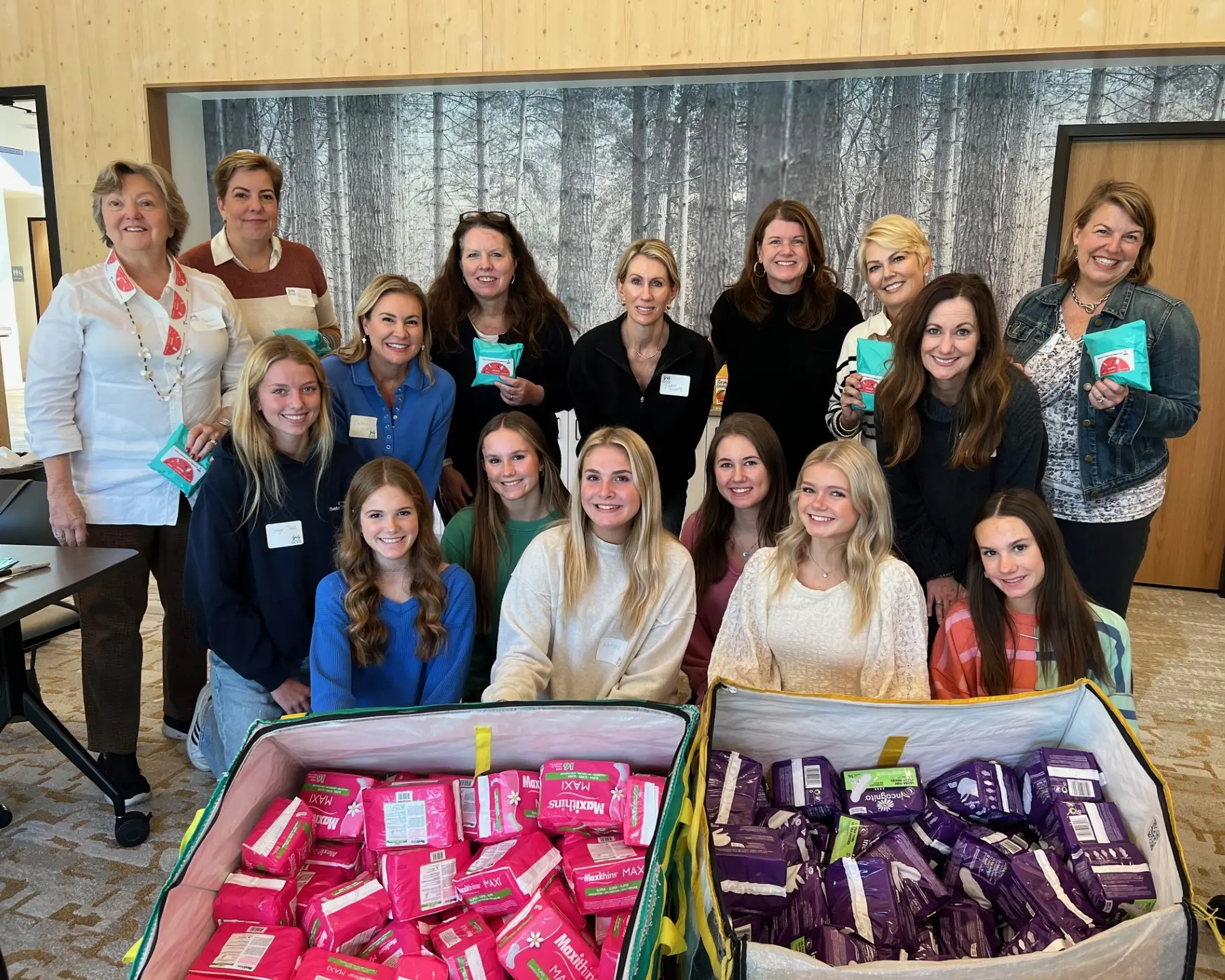 Young women volunteers with Girls Give pose with bins of sanitary pads at a CRC volunteer event.