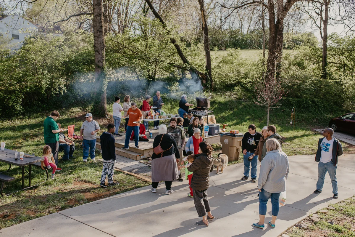 A large and diverse group of all ages enjoy an outdoor cookout.