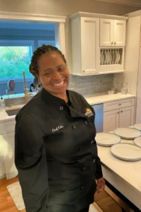 Chef Lola poses smiling in front of rows of empty dishes on an island in a kitchen