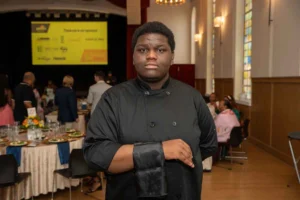 A Pathway participant poses at an event, dressed in all black with a black serving towel draped over his arm.
