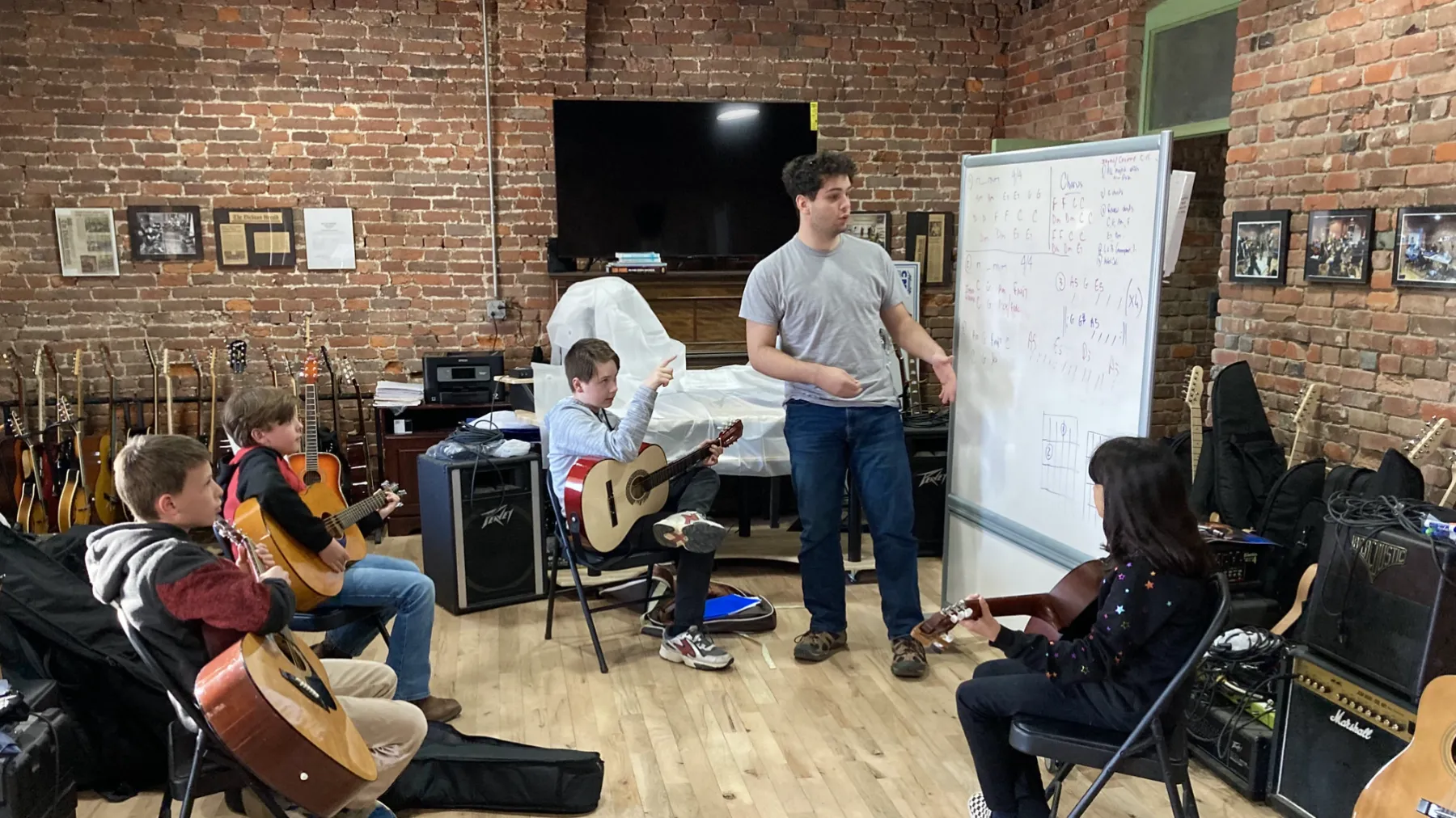 A teacher reviews musical notes with a class full of young guitarist at the Quest Center