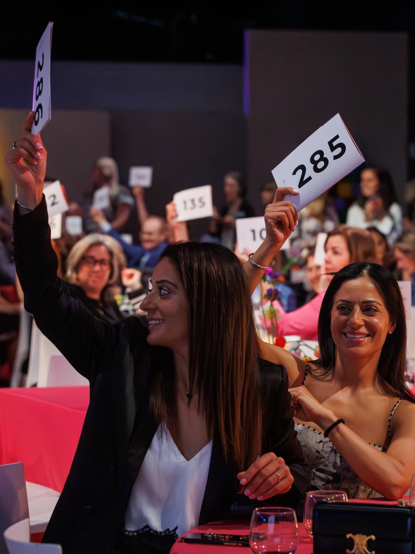 A table of women hold up numbered bidding cards during the auction portion of The Power of the Purse fundraising event hosted by The Women's Fund.