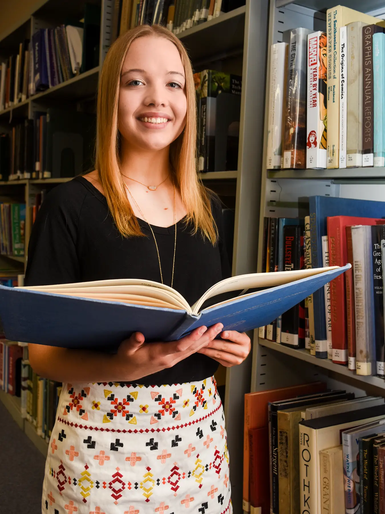 Rachel, a CFMT scholarship recipient, stands in a library with an open book.
