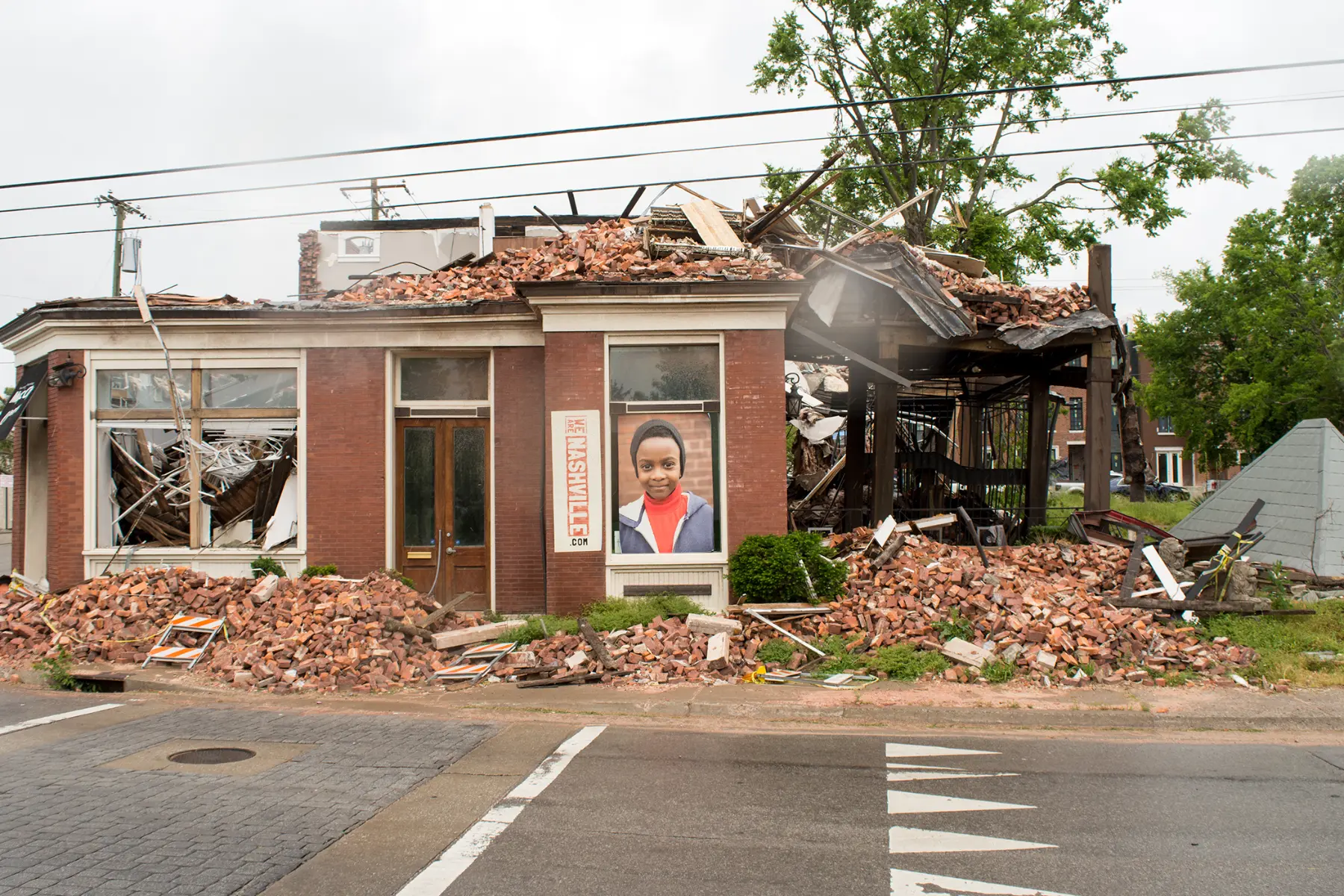 An almost completely destroyed business with the second floor missing and half of the first floor collapsed, has a photo of a young boy in the window and