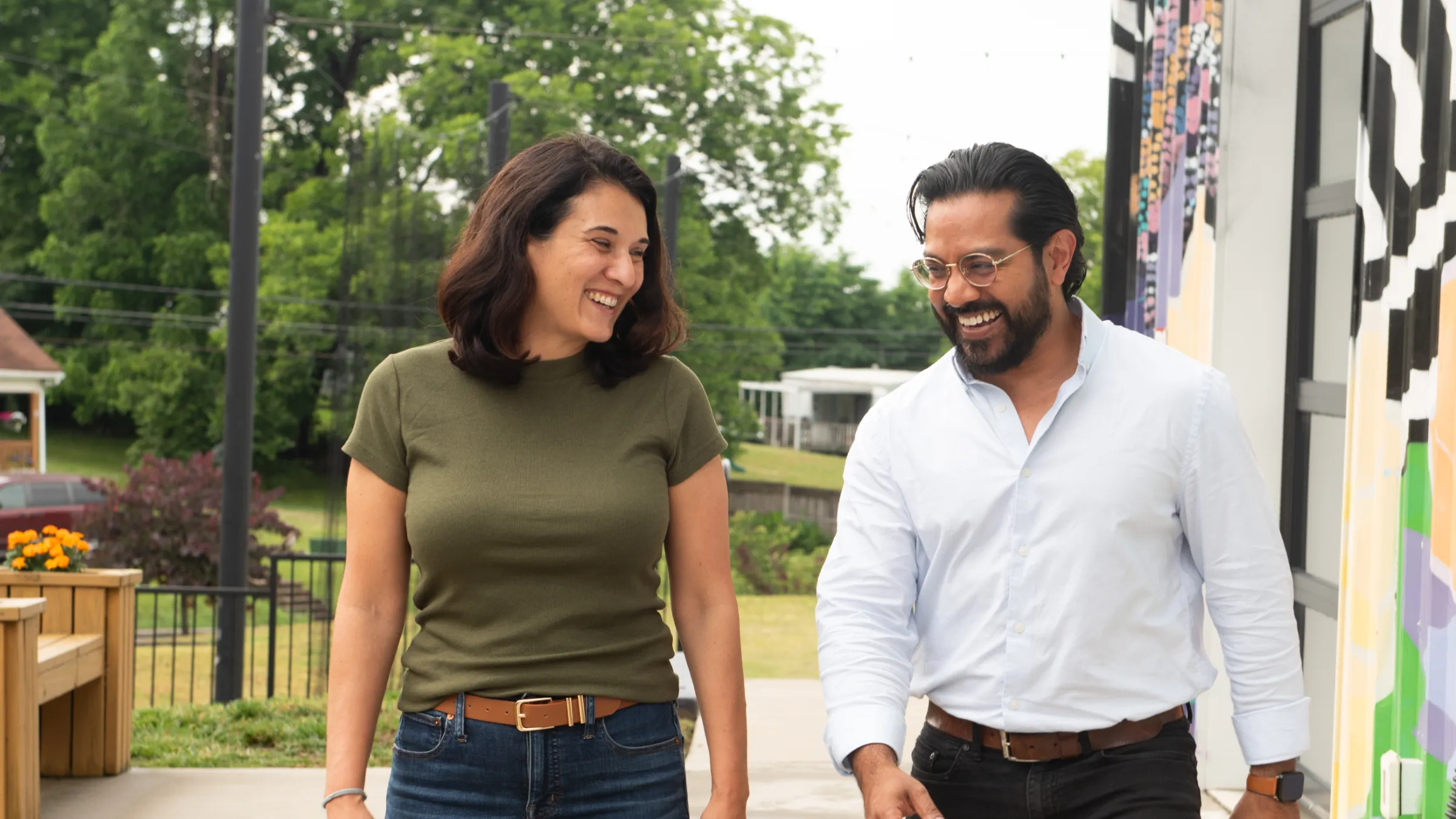 Adnan Karim and Lisa Sherman Luna walk laughing next to each other in front of an art mural.