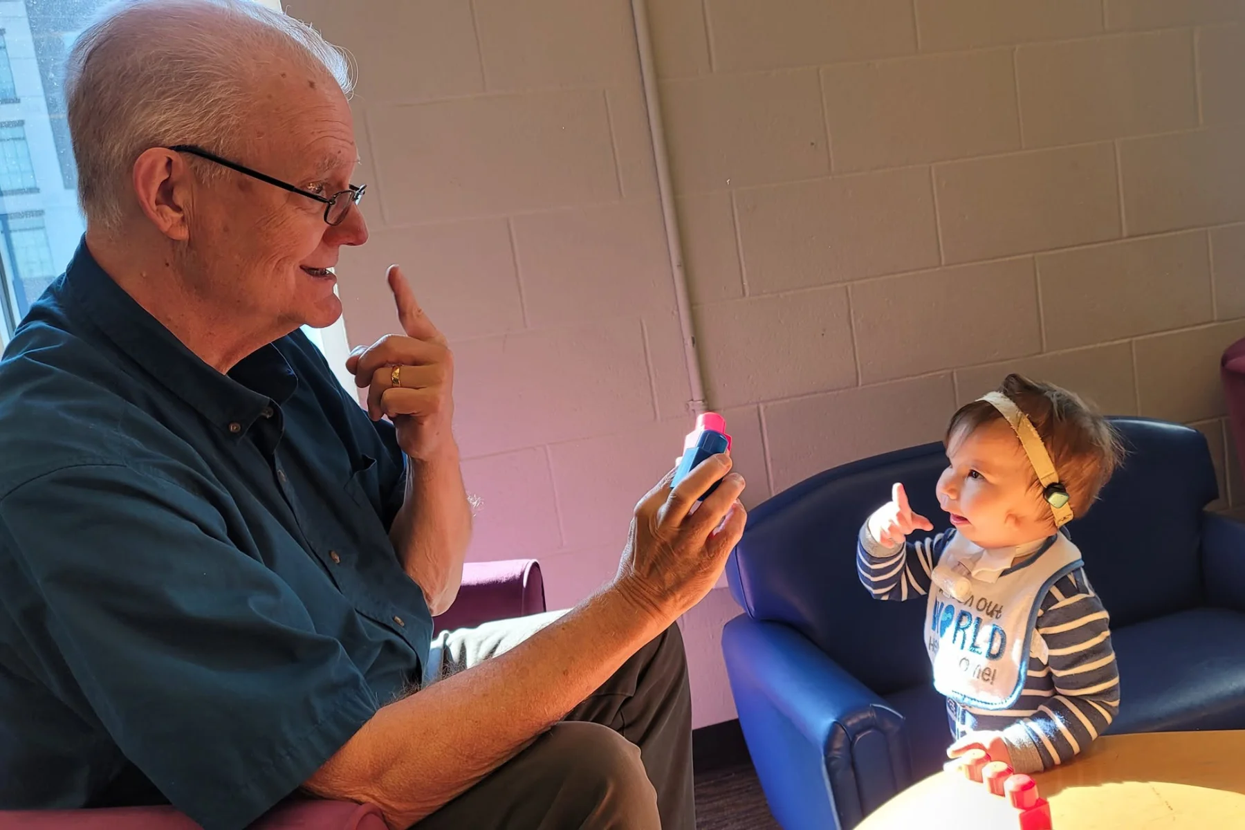 An older man holds a toy working on communication skills with a young girl who is signing back